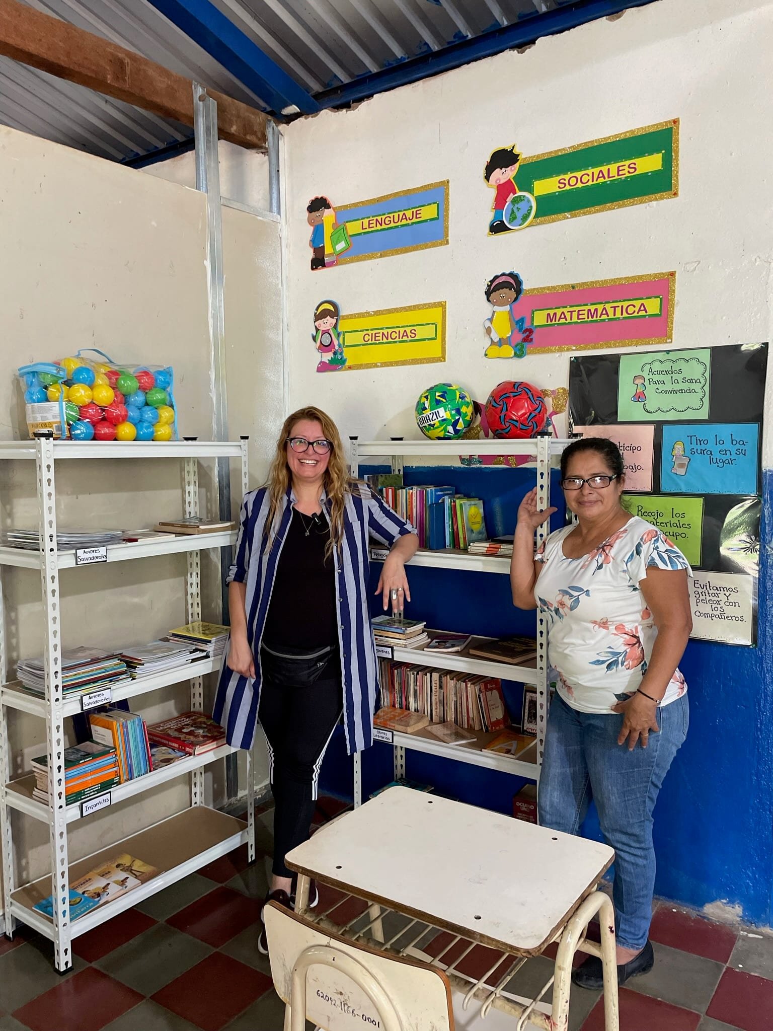 Ana Avilés and a teacher beside the stocked shelves of the new school library