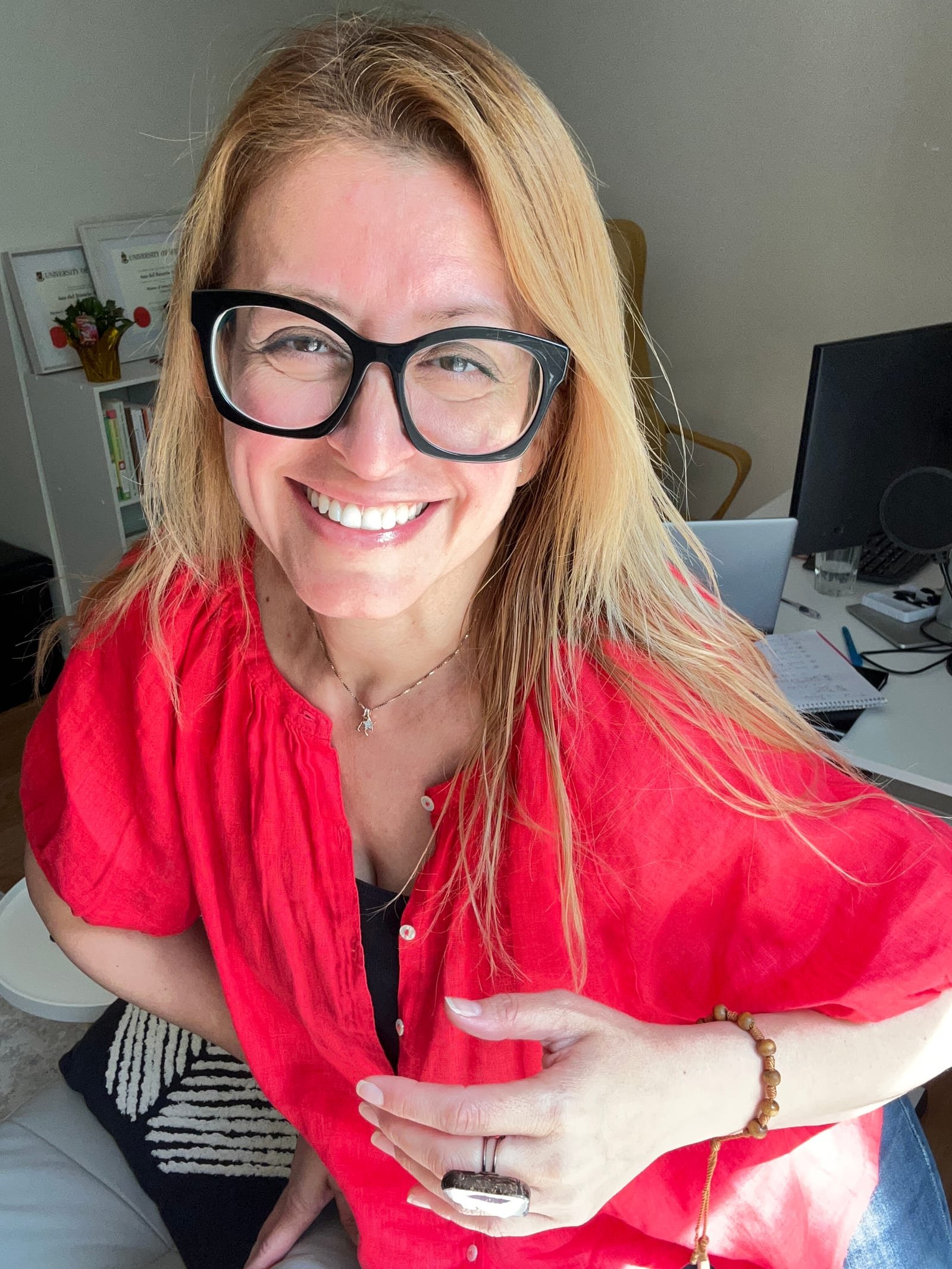 Ana Avilés smiling at the camera in her office, a microphone and monitor on the desk behind her